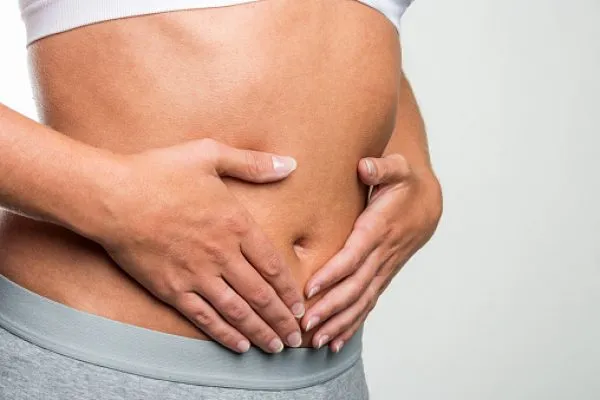 Corpo de mulher que mostra as mãos na sua barriga.